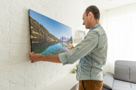 interior decoration and renovation concept - smiling man hanging picture in frame to wall at home