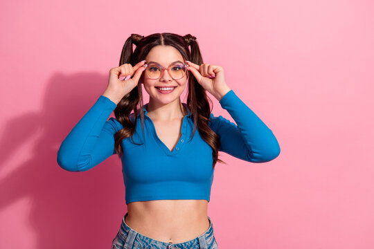 Fototapeta Smiling young woman with stylish glasses adjusting her frames against a pink background, expressing joy and confidence