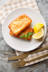 Saganaki is a Greek appetizer consisting of pan-fried cheese served with a lemon wedge, close-up on a plate at the table. Vertical top view from above