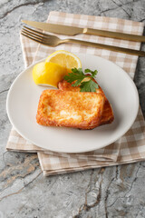 Light Greek appetizer Saganaki of fried cheese served with a lemon wedge close-up in a plate on the table. Vertical