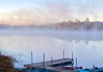 Foggy morning in autumn with lake, fall foliage, and dock with boats