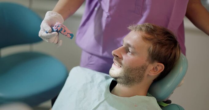 Patient receiving dental care in a modern dental office with a dentist holding a dental mold. The man appears relaxed and comfortable in the dental chair during the consultation.