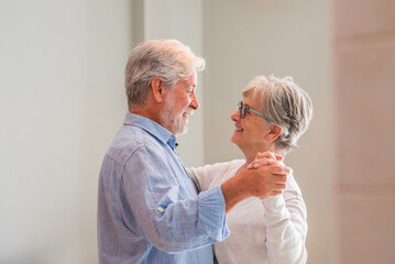 Joyful active old retired romantic couple dancing laughing in living room, happy middle aged wife and elder husband having fun at home, smiling senior family grandparents relaxing bonding together