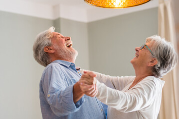 Joyful active old retired romantic couple dancing laughing in living room, happy middle aged wife...