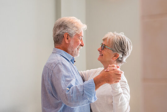 Joyful active old retired romantic couple dancing laughing in living room, happy middle aged wife and elder husband having fun at home, smiling senior family grandparents relaxing bonding together - Powered by Adobe