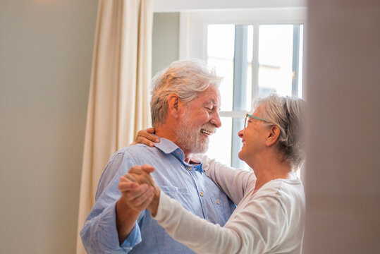 Joyful active old retired romantic couple dancing laughing in living room, happy middle aged wife and elder husband having fun at home, smiling senior family grandparents relaxing bonding together