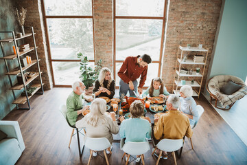 Family gathers around a long dinner table for a joyful Thanksgiving feast with grandparents parents...