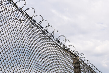 Metal fence with barbed wire under cloudy sky. Security and protection concept. Restricted area boundary. Prison or military facility detail. Safety and control symbol. Freedom limitation idea.
