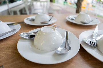 Multiple white bowls are placed upside down on plates with spoons on a wooden table in a restaurant.