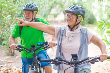 Two happy old mature people enjoying and riding bikes together to be fit and healthy outdoors. Active seniors having fun training in nature. Portrait of one old man smiling in a bike trip with wife © Daniel