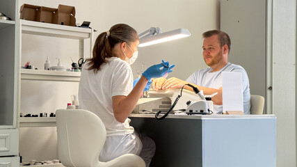 A meticulous Caucasian woman beautician meticulously tends to a Caucasian man's nails, evoking spa tranquility and Hygge comfort traditions