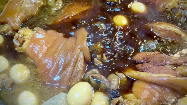 Traditional Thai-style braised pork leg simmering in a rich dark soy and herbal broth with boiled eggs. Authentic Asian street food captured in close-up detail.