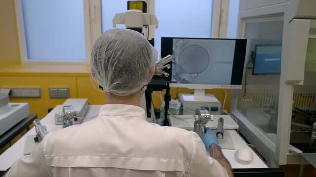 Performing artificial fertilization procedure using a microscope at a clinic. Looking at the human egg fertilization in a microscope at clinic. Clinic doctor examines the fertilization with microscope
