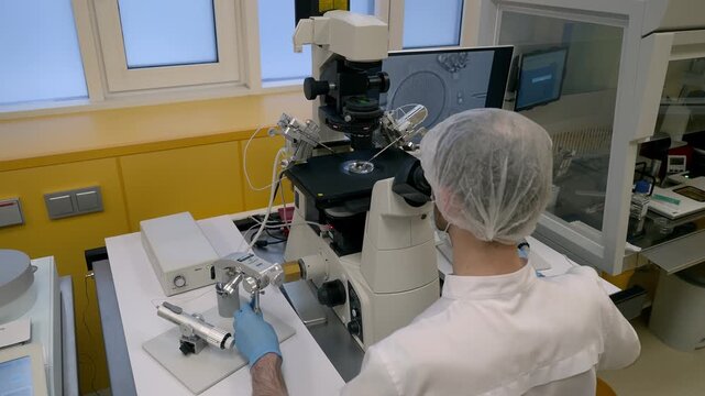 Medical Clinic Doctor Adjust Knobs On Microscope To Examine Patient's Sample. Embryologist Analyzing Cells Using Modern Medical Clinic Microscope. IVF Microscope. Maternity Clinic. Medical Concept
