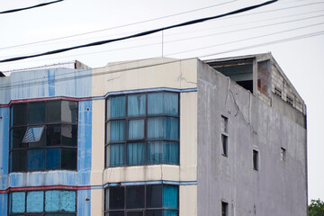 An old, weathered multi-story building with faded paint, large bay windows, and power lines against an overcast sky