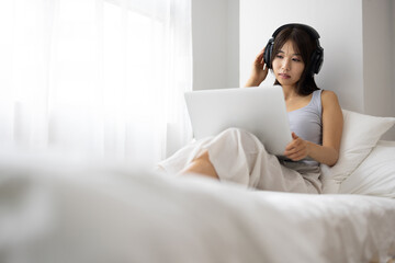 Young Woman Watching Laptop with Headphones in Bed