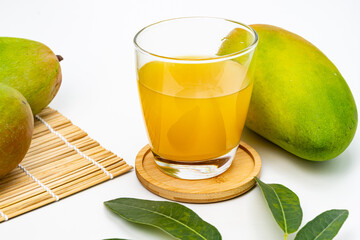 A refreshing glass of freshly squeezed mango juice is placed among ripe mangoes and green leaves.