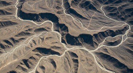 Aerial view of a winding river and roads through arid, rugged mountain terrain with dramatic shadows