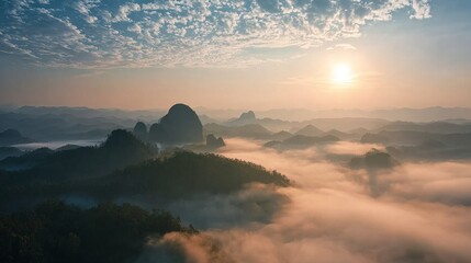 A serene sunrise illuminates mist-covered karst mountains, creating a dreamy and ethereal landscape.