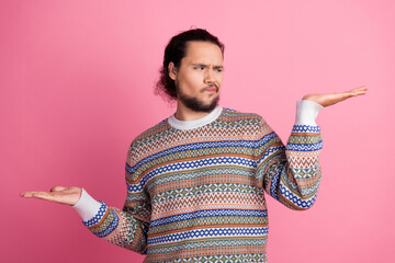 Young man wearing colorful patterned sweater making expressive hand gestures against a pink background