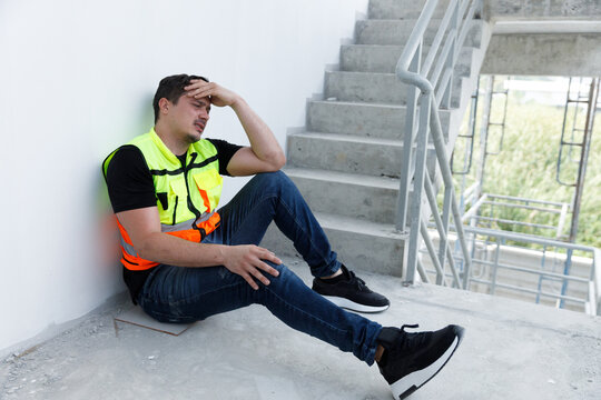 Construction worker in safety vest sitting on stairway with hands on head, showing signs of stress, fatigue, or headache. Concept of burnout, job pressure, mental health, and labor exhaustion.