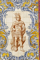Fototapeta premium azulejos tile mural depicting a man in elaborate period clothing, including a green tunic with gold accents, blue pants, and a feathered hat in Setubal, Portugal