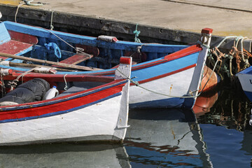 Obraz premium Two small wooden boats docked at a concrete pier, painted white with red and blue accents in Setubal, Portugal