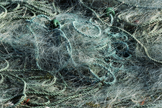 Large pile of tangled fishing nets and ropes spread across a dock near water in Setubal fishing port, Portugal - Powered by Adobe
