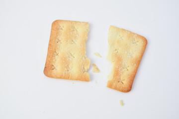 Single cracker broken in half with crumbs on white background, minimalist food composition highlighting crispy texture, suitable for snack, bakery, or advertising use.