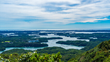 A spectacular view of the Ago Bay rias coast from the Yokoyama Observation Deck, featuring lush green islands and a calm sea dotted with aquaculture rafts. It symbolizes the natural beauty of Japan.