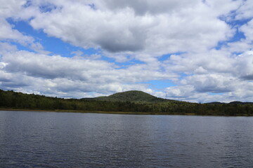 A panoramic view of a solitary idyllic lake nestled in the Adirondacks covered by fluffy clouds and blue skies.