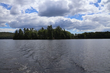 A panoramic view of a solitary idyllic lake nestled in the Adirondacks covered by fluffy clouds and blue skies.