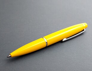 Yellow ballpoint pen with silver clip on gray surface.