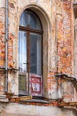 Weathered arched doorway with old wooden door, destroyed balkony, peeling paint and exposed brick