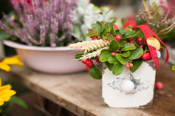 Preetz, Schleswig-Holstein, Germany, 2025/10/14 A bright floral arrangement in a green pot with red and pink flowers, decorated with a gingham ribbon and autumn accents, placed on a rustic wooden tabl