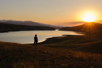 Silhouette of a woman on a hill enjoying the picturesque view of the mountains and water at sunset. Peace and quiet.