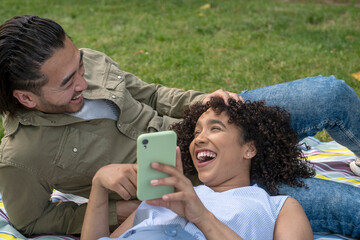 Interracial couple laughing while watching smartphone outdoors