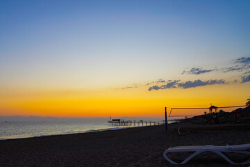 A Serene Beach Scene at Sunset with Vibrant Colors in the Sky Reflecting Over Calm Waters and Silhouetted Structures Along the Shoreline