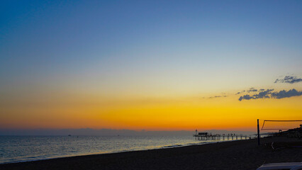 A Serene Evening at the Beach: Captivating Colors of Sunset Reflecting on the Calm Ocean with a Pier in the Distance