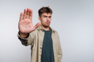 Naklejka premium Young man raises hand to signal stop against a plain background in a casual indoor setting