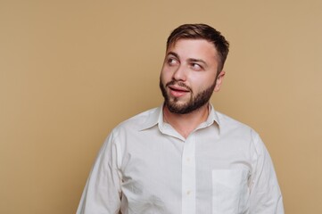 Man with beard wearing a white shirt gazes thoughtfully toward the side against a solid background