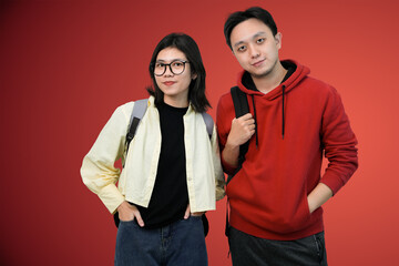friendly students pose with backpacks pose together against bright red background in casual youthful portrait