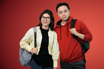 friendly students pose with backpacks pose together against bright red background in casual youthful portrait
