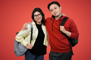 Fototapeta premium friendly students pose with backpacks pose together against bright red background in casual youthful portrait