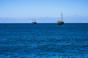 Two Sailboats Gliding Across a Serene Ocean under a Clear Sky, with Mountains Distantly Framing the Horizon