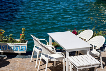 A Tranquil Waterfront Scene Featuring White Furniture and Calm Waters Surrounded by Lush Greenery and Colorful Flowers