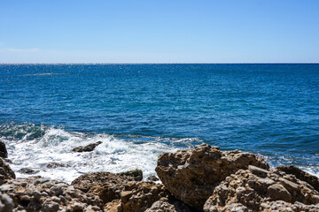A Tranquil Coastal Scene with Lapping Waves Against Rocky Shoreline Under Clear Blue Skies Reflecting the Beauty of Nature's Harmony