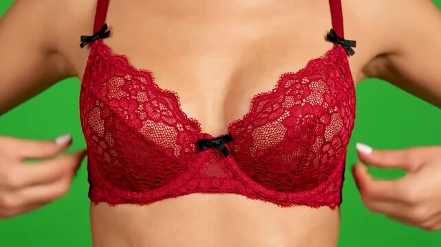 Close-up of a womans torso wearing a red lace bra against a green screen.