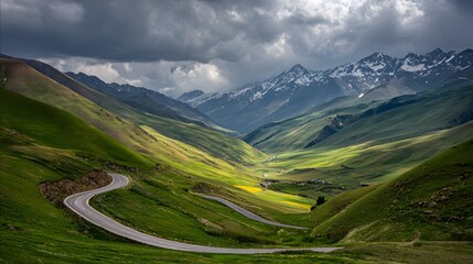 Fototapeta premium Winding road through a verdant mountain valley under dramatic clouds.