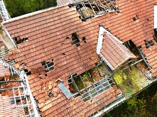Aerial view of abandoned building with collapsed roof surrounded by forest